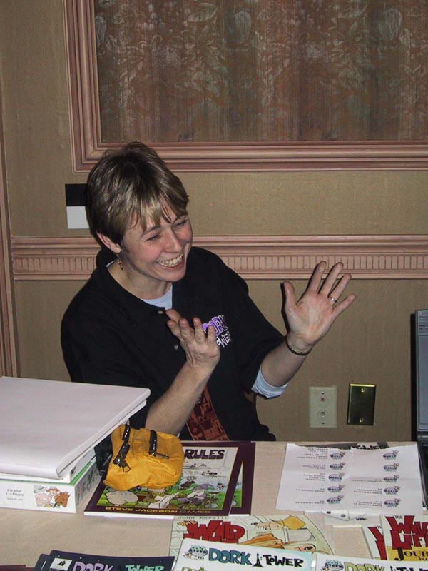 woman with big grin gestures at a table of comics